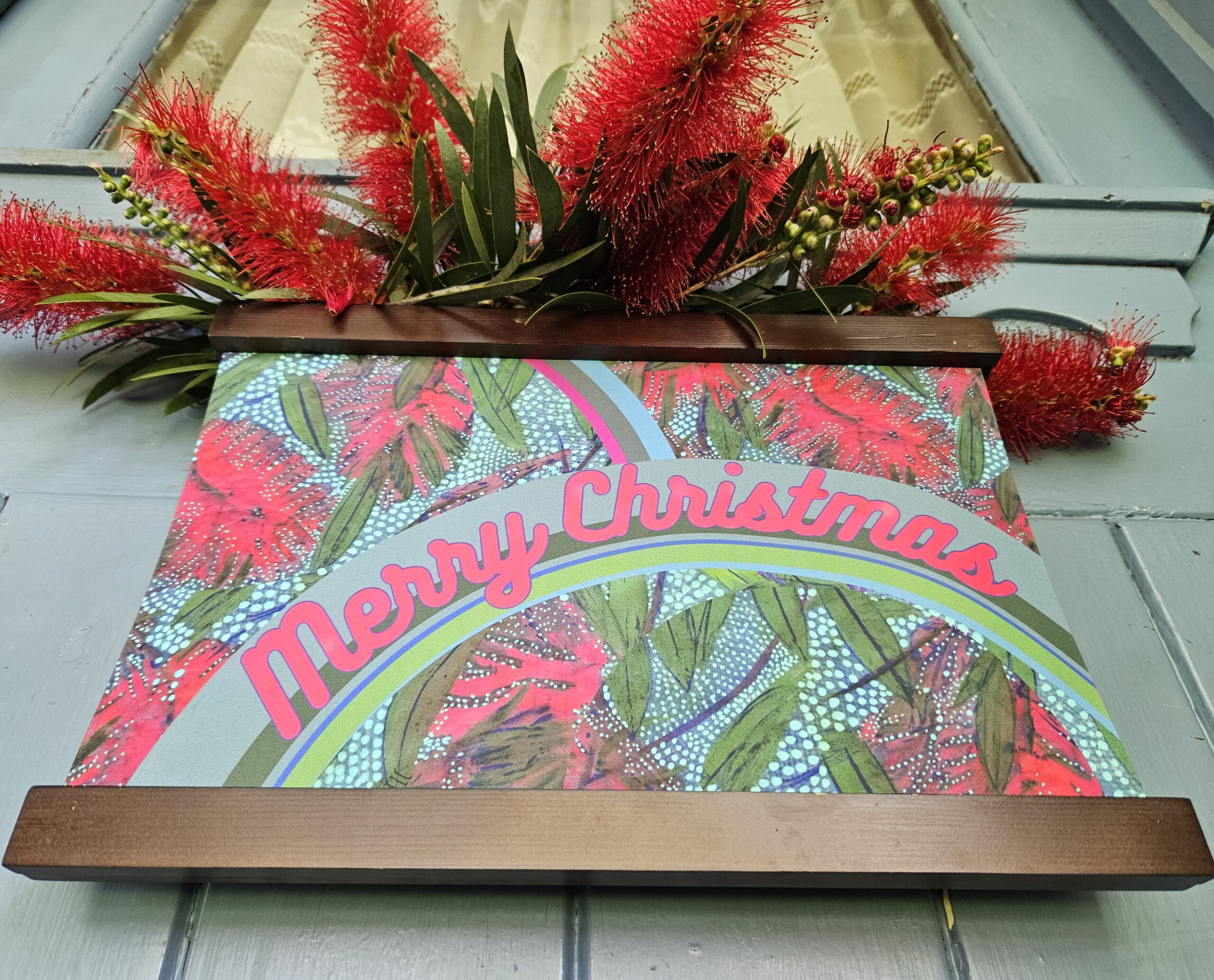 a Merry Christmas welcome door hanger poster, with red cursive writing and Australian Bottlebrush design, decorated with bottlebrush flowers