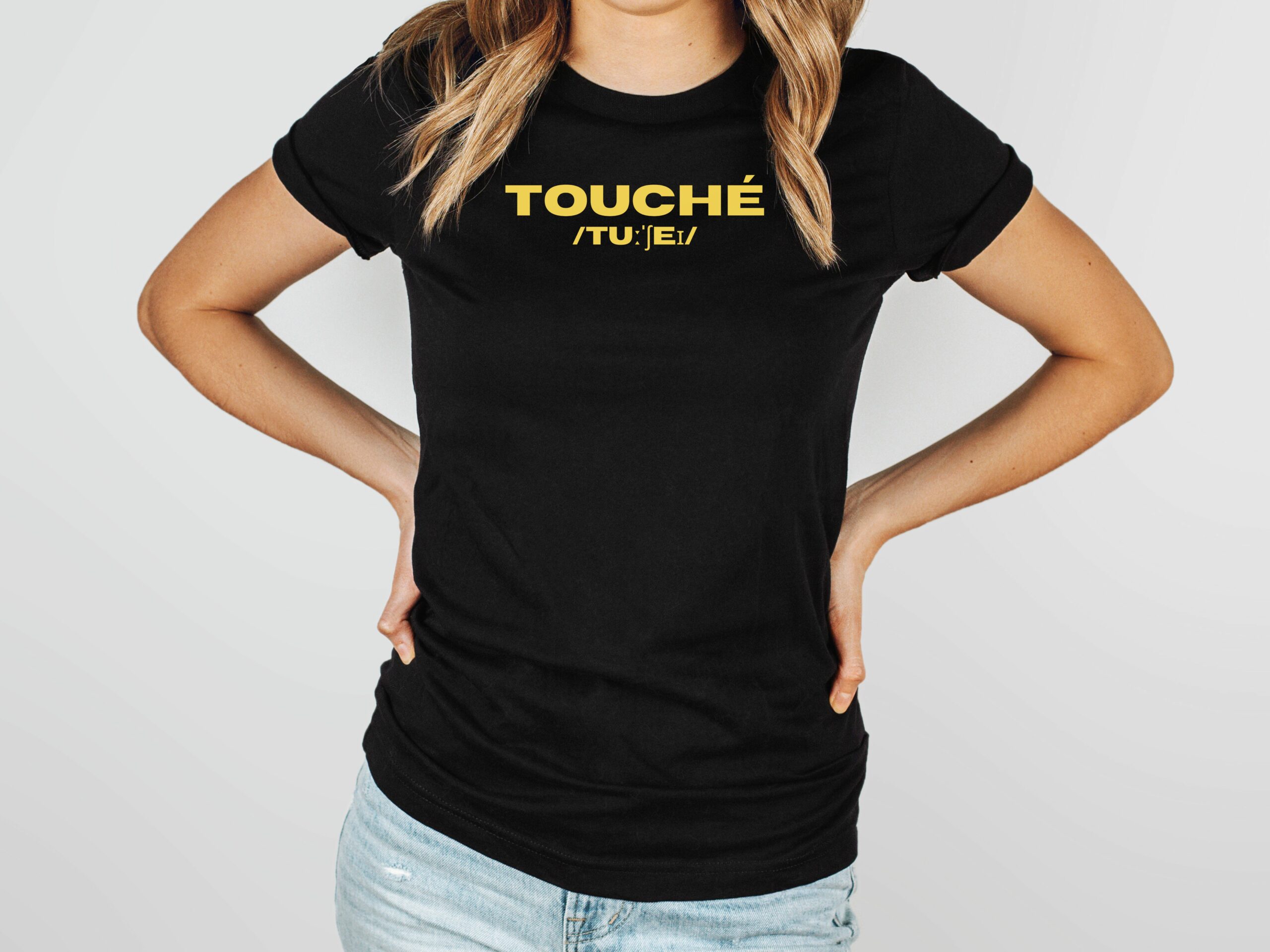 A woman in a black t-shirt with the word Touché and it's phonetic notation in yellow